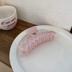 Détail de la pince à cheveux rose mat avec design de chaîne sur un plateau blanc