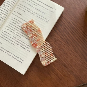 French wavy acetate wide-tooth hair comb with elegant marble texture on a book