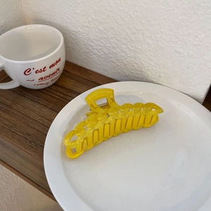 Détail d'une pince à cheveux jaune vif style chaîne posée sur une assiette en céramique