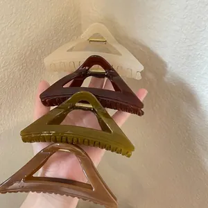 Triangle acrylic hair claw clips in four colors shown being held in hand