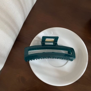 Deep forest green rectangular hair claw clip with golden spring on white ceramic plate