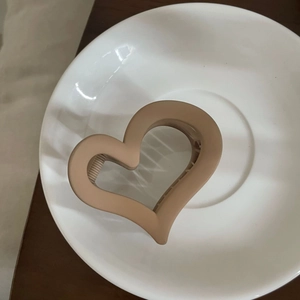 Nahaufnahme der mattbeigen herzförmigen Haarklammer auf einem weißen Keramikteller für Damen