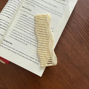 Close-up of elegant wavy marble hair comb resting on an open book over a wooden desk