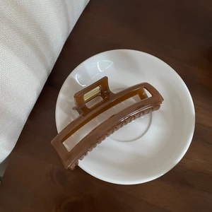 Detailed shot of a brown rectangular hollow hair claw clip on a white ceramic plate