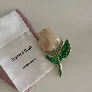 Enamel tulip hair claw clip in creamy white and green on a minimalist sachet background