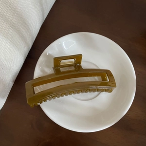 Detail view of a caramel resin hair claw clip with a rectangular hollow design in a ceramic dish