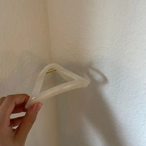 Creamy white triangular acrylic hair claw clip with golden spring held by hand