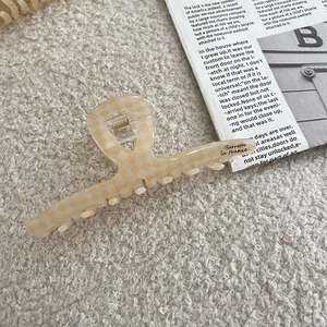 Vue détaillée d'une grande pince à cheveux à carreaux beige en acétate sur peluche