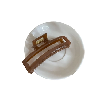 Elegant brown rectangular hair claw clip with gold spring on a minimalist white ceramic plate