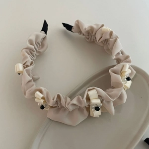 Elegant cream pleated headband with small bows and beaded accents on ceramic tray