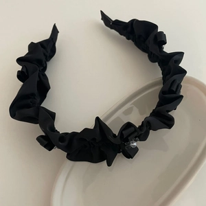 Elegant black pleated headband with satin finish and sparkling crystal beads on white tray