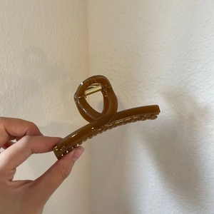 Detail of a brown acrylic hair claw clip showing its spring and non-slip wavy teeth