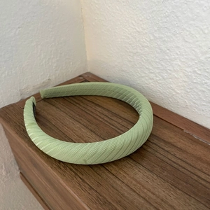 Light green striped wide headband with pleated texture on a wooden surface