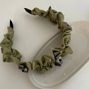 Elegant olive green pleated satin headband with grey bow and crystal beads on ceramic tray
