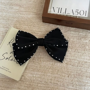 Elegant black bow hair clip with pearls and rhinestones on a minimalist fabric background