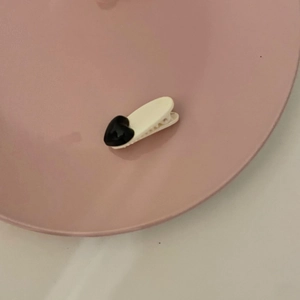 Detailed top view of a black heart hair clip on a white duckbill base shown on a pink tray