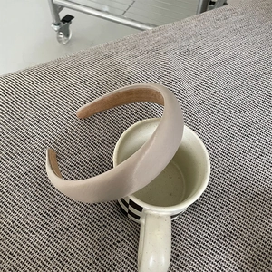 Padded khaki satin headband for women with non-slip lining on a white ceramic mug
