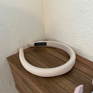 Detail of a beige pleated fabric headband with a black Hand Made label on a wooden surface