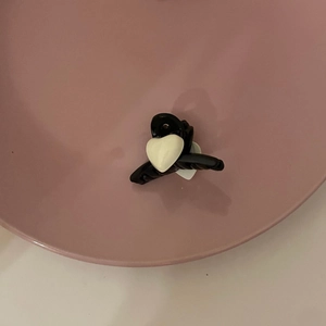 Detail shot of mini black hair clip with white heart motif in a pink decorative tray