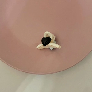 Vintage heart hair clip in cream and black resin, shown on a pink ceramic plate