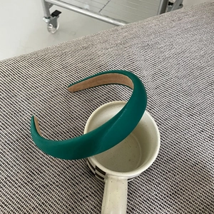 Top view of dark green padded satin headband on a checkered cup with non-slip lining