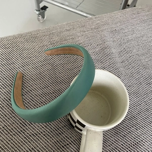 Detail of a wide dark green satin headband resting on a checkered ceramic cup