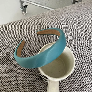 Close-up of a padded peacock blue satin headband with brown non-slip inner lining