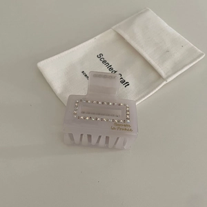 Detail of square acetate hair claw with rhinestones and branded canvas gift bag