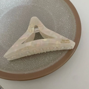 Gros plan sur la pince à cheveux triangulaire en acétate avec marbrure crème et texte doré