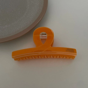 Detail view of large orange acetate hair claw clip featuring a French design and metal spring
