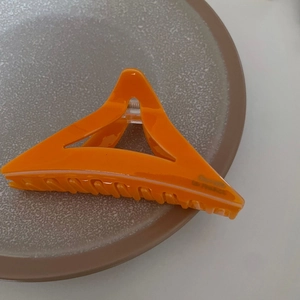 Détail d'une pince à cheveux triangulaire orange vif avec une finition en acrylique