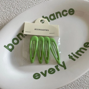 4-piece set of bright green water drop metal hair clips in packaging on ceramic plate