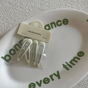 Close-up of four mint green BB hair clips on an ivory card inside a ceramic tray