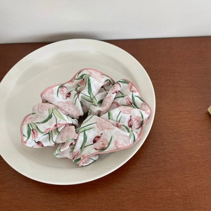 Gros plan sur un chouchou à imprimé tulipes roses et feuilles vertes sur une assiette blanche