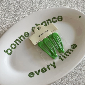 Three green drop-shaped BB hair clips displayed on an accessory card in a ceramic tray