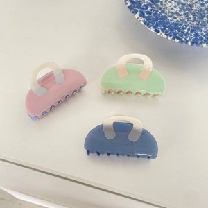 Three acetate shark hair claws in pink, mint green and blue on a white surface