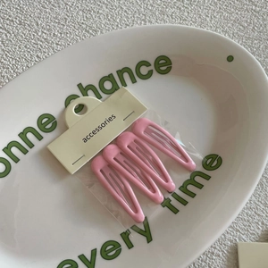 Close-up of four pink cream-colored drip oil hair clips on a card inside a poly bag