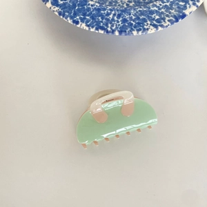 Minimalist light green acetate shark hair claw clip for women on a clean white desk
