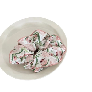 Chouchou géant avec motif de tulipes roses, rubans et tissu floral sur un plat blanc épuré