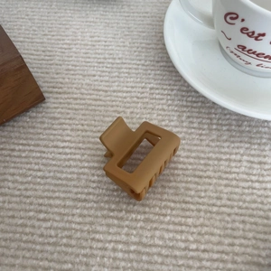 Détail macro d'une petite pince à cheveux carrée en acrylique marron mat sur tissu