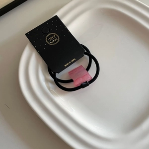 Détail d'élastique à cheveux rose en acrylique sur carte noire et plateau blanc