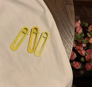 Gros plan de trois pinces à cheveux jaunes mates sur tissu blanc avec fond floral
