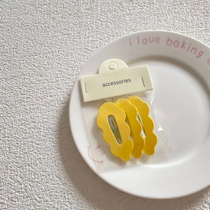 Three-piece set of yellow matte wavy hair clips with packaging on a ceramic plate