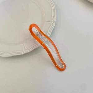 Vibrant orange and transparent wavy macaron hair clip on a white ceramic plate
