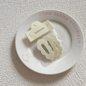 Close-up of three cream wave-edged hair clips on a ceramic plate with packaging