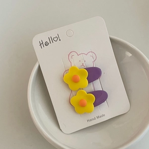 Detail view of two cute purple matte hair clips with yellow floral charms on a white card