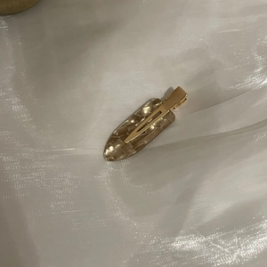 Flat lay of a light brown marble acetate duckbill hair clip on white silk fabric