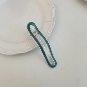 Detail view of a dark green acrylic hair clip with a gold metal spring on a ceramic plate