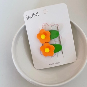 Close-up of two cute orange flower hair clips on a decorative handmade paper card
