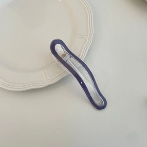 Detailed view of a wave-shaped purple and clear acrylic hair clip on a ceramic tray